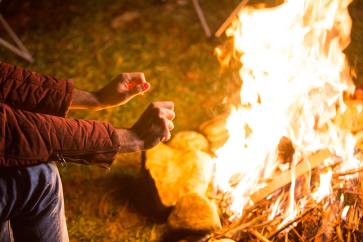 young-man-warming-up-his-hands-bonfire-campsite-mountains